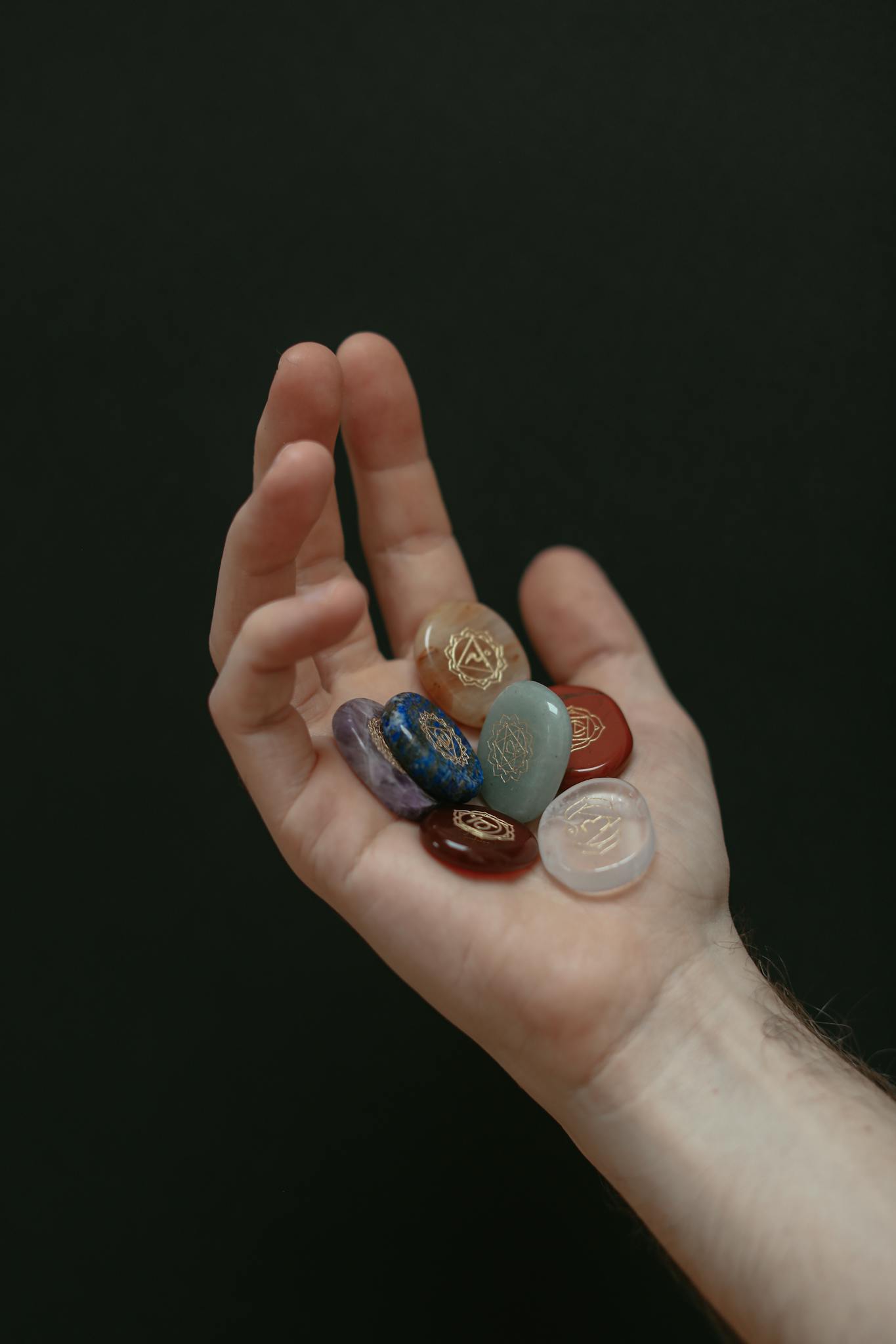 A hand holding a variety of colorful gemstones against a black background.