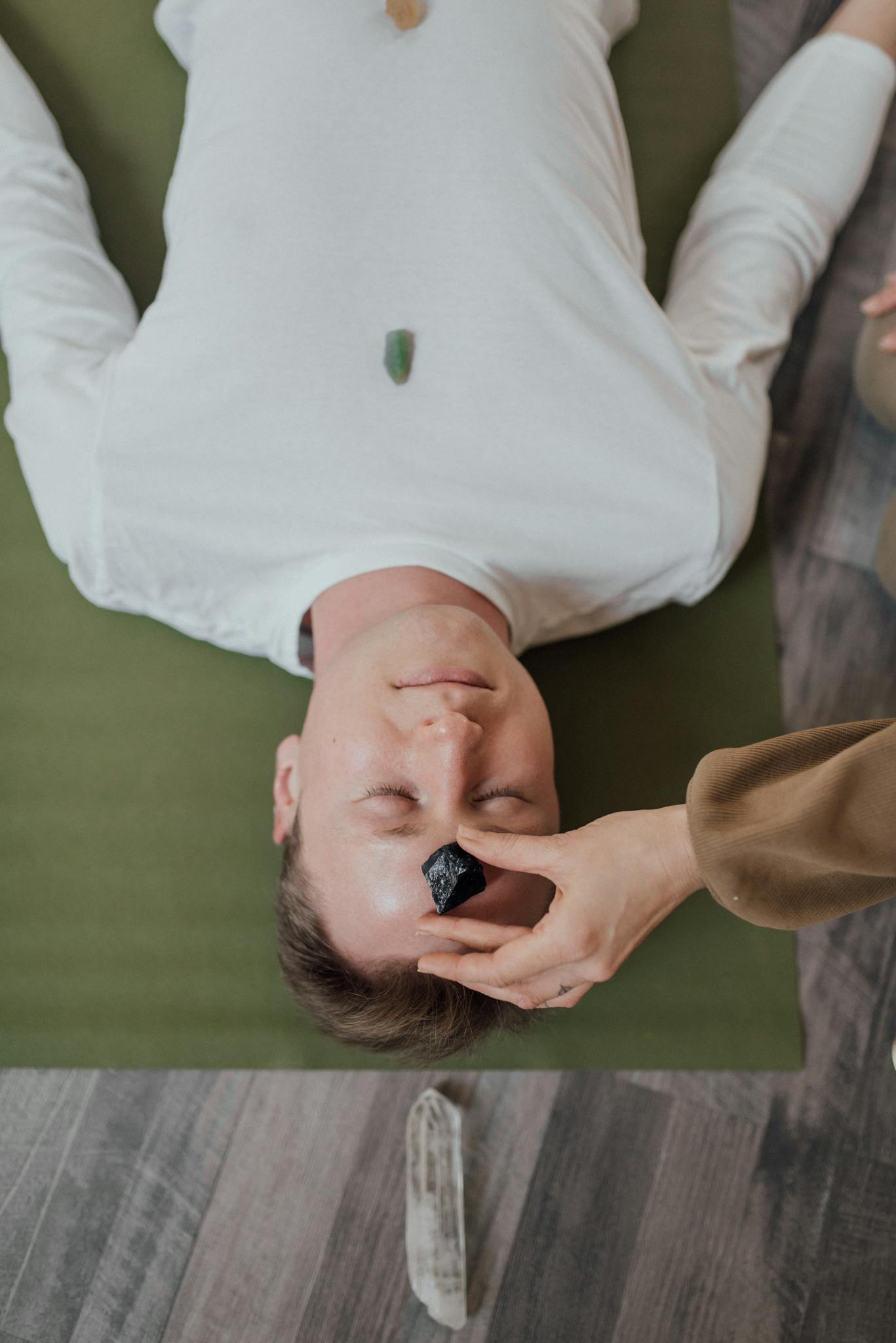 Man lying on mat with healing minerals, receiving a relaxing crystal therapy session indoors.